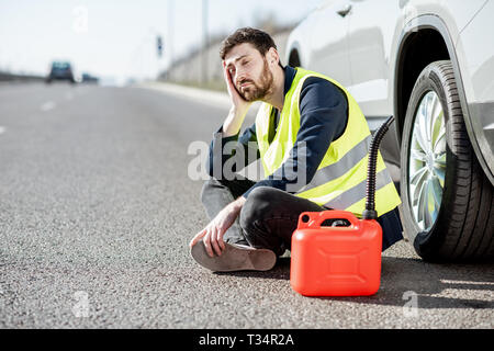 Homme avec désespoir émotions assis avec le plein de sa voiture près de la cartouche sur le bord de la route Banque D'Images