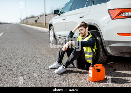 Homme avec désespoir émotions assis avec le plein de sa voiture près de la cartouche sur le bord de la route Banque D'Images