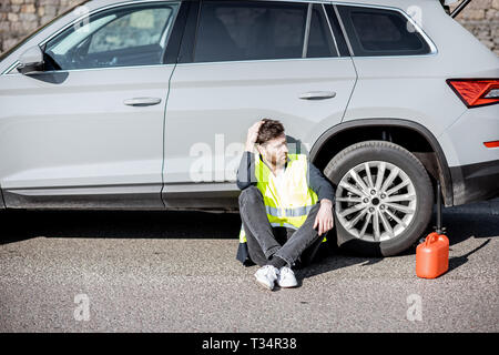 Homme avec désespoir émotions assis avec le plein de sa voiture près de la cartouche sur le bord de la route Banque D'Images