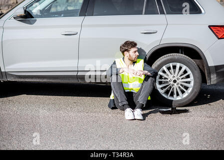 Homme avec désespoir en attente d'émotions l'assistance routière assis près de la voiture sur le bord de la route Banque D'Images