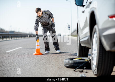 L'assistance routière d'urgence mettre travailleur près du cône sur l'autoroute voiture cassée Banque D'Images