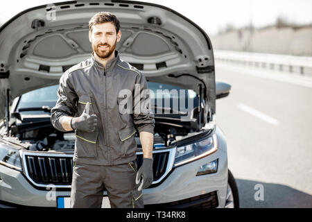 Portrait of a handsome travailleur d'assistance routière en uniforme à l'extérieur de la voiture sur le bord de la route Banque D'Images