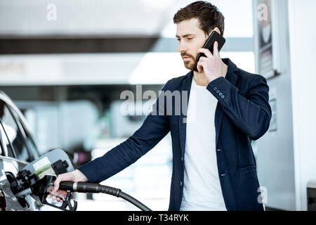 Couple avec téléphone lors d'un plein à la station d'essence de voiture Banque D'Images