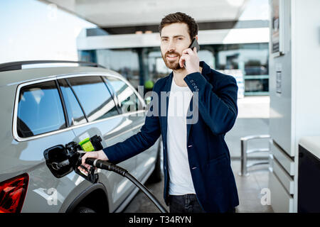 Couple avec téléphone lors d'un plein à la station d'essence de voiture Banque D'Images