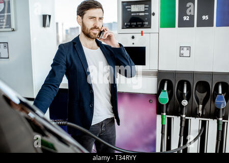 Couple avec téléphone lors d'un plein à la station d'essence de voiture Banque D'Images