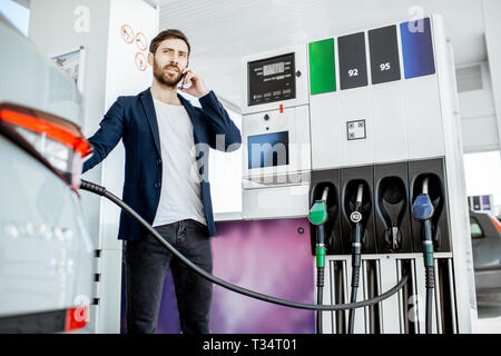 Couple avec téléphone lors d'un plein à la station d'essence de voiture Banque D'Images