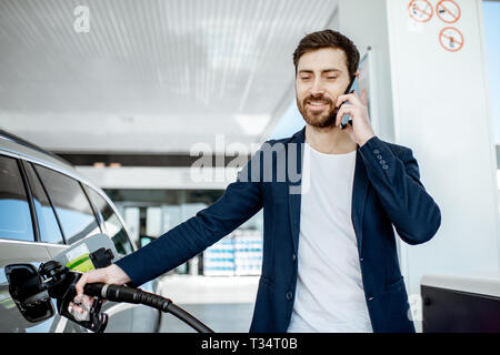 Couple avec téléphone lors d'un plein à la station d'essence de voiture Banque D'Images