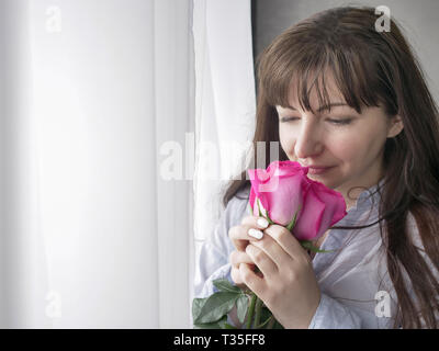 Jeune femme renifle un bouquet de roses par la fenêtre permanent Banque D'Images