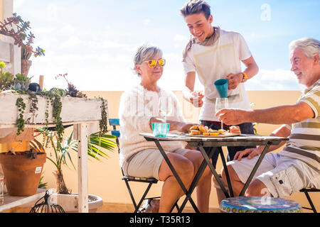 Adultes et grands-pères matures adolescent neveu, pratiquer des activités de plein air sur la terrasse avec loisirs certains aliments et boissons. L'océan et vue sur la ville, locations journée ensoleillée Banque D'Images