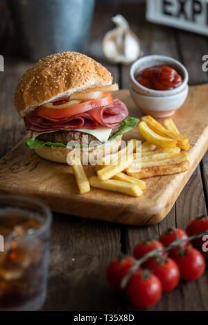 Burger et frites sur planche de bois placée sur une table en bois rustique avec un verre de soda sur le côté , et les petits du ketchup Banque D'Images