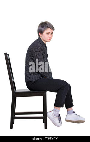 Side view full length portrait de jeune femme fatiguée assis sur une chaise à déçu à l'appareil photo isolated over white background. Banque D'Images