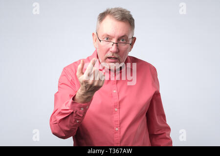 Man grave duscussing en chemise rouge question avec vous avec les mains ouvertes. Studio shot. Le langage du corps ou du visage l'émotion humaine Banque D'Images