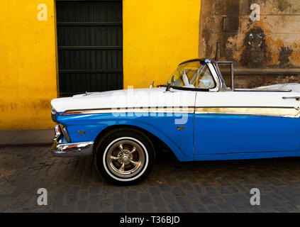 Blanc et bleu 1957 Ford Fairlane 500 Sunliner Convertible en stationnement sur rue pavée à fond jaune mur dans la Havane, Cuba Banque D'Images