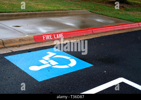Parking Handicap avec fauteuil roulant apposé à côté d'un feu, dans un parc de stationnement sur un jour de pluie. Banque D'Images