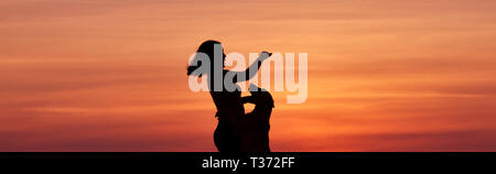 Silhouettes au coucher du soleil, une fille et un chien dans le contexte d'un incroyable coucher du soleil, un chien de berger belge Malinois, jouant et sautant Banque D'Images