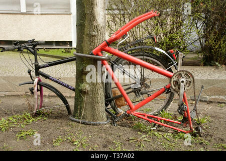 Vieilles bicyclettes vandalisée avec de nombreux composants manquants mais toujours verrouillé sur un arbre, Berlin, Allemagne. Banque D'Images