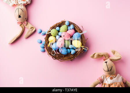 La décoration des œufs de Pâques colorés dans un nid et les lapins sur fond rose pastel. Mise à plat Banque D'Images