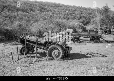 Rusty old tracteur, voiture et remorques agricoles assis dans l'herbe verte dans la cour sur le terrain au début du printemps, journée ensoleillée, l'arrière-plan avec leadless f Banque D'Images