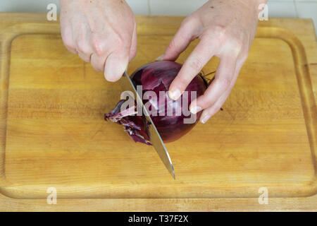 Close up of female trancheuse se termine au large d'un oignon rouge sur une planche à découper. Banque D'Images