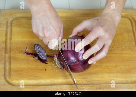 Close up de dessus de trancher les extrémités d'un oignon rouge sur une planche à découper. Banque D'Images