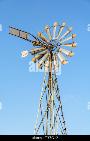 Low angle view of an old-fashioned, multi-lames, metal pompe éolienne au sommet d'un pylône en treillis contre le ciel bleu. Banque D'Images