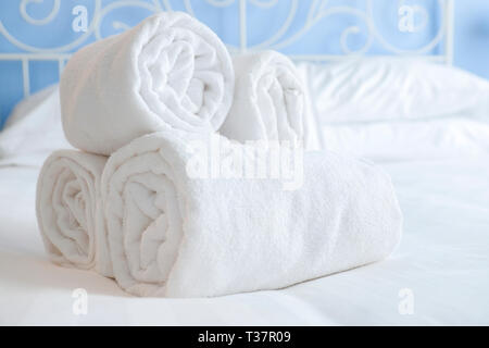 Bien roulé des serviettes propres et s'allonger sur les draps blancs d'un lit d'acier dans une chambre d'hôtel magnifiquement éclairée Banque D'Images