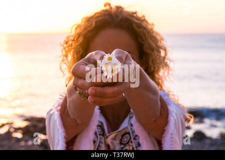 Amour de la nature et de l'environnement concept avec curly libre prenant et montrant un groupe de marguerites avec les mains - coucher du soleil à backli Banque D'Images
