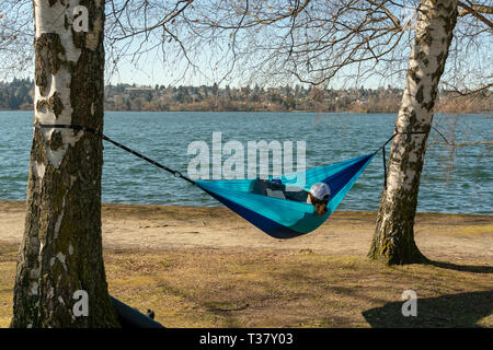 Seattle, Washington - 2019-03-17 - femme lisant un livre dans un hamac pendu à partir d'un couple d'arbres à Greenlake le printemps commence à Seattle Banque D'Images