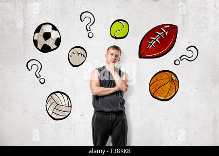 Vue avant du jeune homme en veste à capuche sans manches avec commandes à menton à main mur avec des dessins de différents sport balls et interrogation parmi Banque D'Images