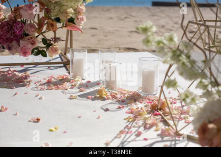 Pétales de fleurs fraîches se trouvent sur le sol près d'une arche de mariage décoration et bougies blanches. La décoration de l'événement avec des fleurs fraîches. Banque D'Images