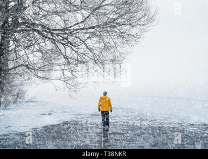 Un homme en manteau jaune marche sur la route couverte de neige Banque D'Images