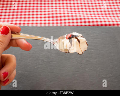 Une femme avec des ongles peints en rouge avec une cuillère dans sa main avec la crème, sauce au chocolat et de couleur chocolat Banque D'Images