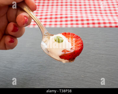 Une femme avec des ongles peints en rouge avec une cuillère à la main avec de la crème, de couleur chocolat et un morceau de fraise Banque D'Images