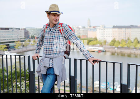 Homme mûr en chapeau de paille avec sac à dos, debout sur une terrasse à Helsinki, Finlande Banque D'Images