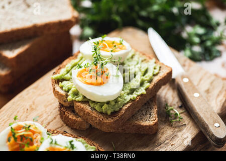 Petit-déjeuner santé toast à l'avocat, oeuf mollet sur planche à découper en bois Banque D'Images