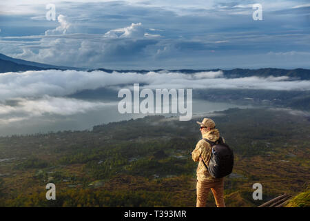 L'homme regarde le lever du soleil sur le volcan Batur sur l'île de Blai en Indonésie. Sac à dos homme Randonneur avec un haut volcan, travel Banque D'Images
