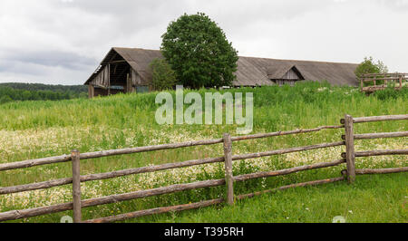 Clôture en bois simple primitive sur la ferme, l'herbe verte, dans l'arrière-plan la vieille structure Banque D'Images