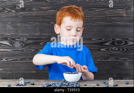 Petit garçon venu cueillir des bleuets dans une assiette dans la cuisine, des couleurs sombres à l'intérieur Banque D'Images