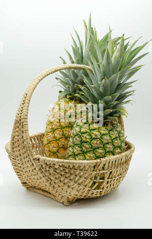 Photo de deux coudées d'ananas avec de grosses tiges dans un panier en osier sur un cas isolé sur fond blanc Banque D'Images