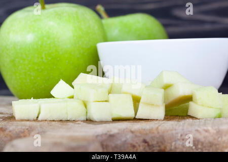 Pelés et coupés en morceaux de pomme verte, un bol blanc sur une planche à découper Banque D'Images