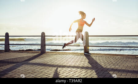 Fit young woman in fonctionne rapidement sur une promenade de bord de mer. Vue de côté de coureuse sprint pendant le coucher du soleil. Banque D'Images