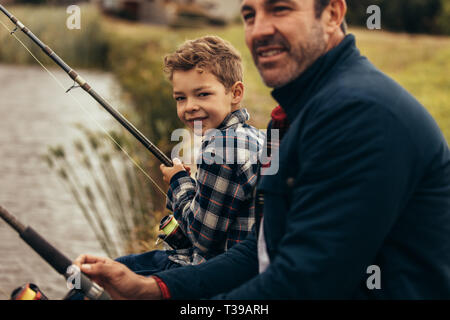 Portrait d'un homme assis sur les rives d'un lac avec son kid holding des cannes à pêche. Père et fils faisant la pêche comme une activité de loisirs. Banque D'Images