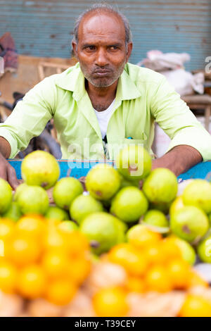 Varanasi, Inde, 10 mars 2016 - fournisseur indien se trouve en face d'un tas de sucre vert frais pommes et oranges Banque D'Images