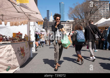 Une jolie femme eating potato chips et marche à travers l'Union Square Green Market à Manhattan, New York City. Banque D'Images