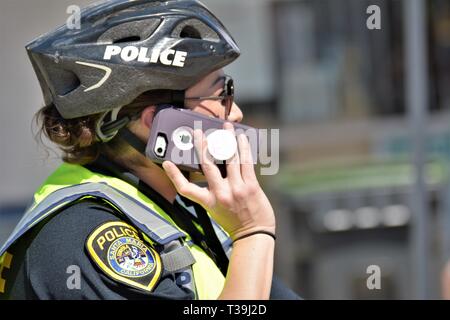 Femme policier sur téléphone cellulaire comme elle est sur patrouille à pied avec casque et gilet de sécurité jaune Banque D'Images