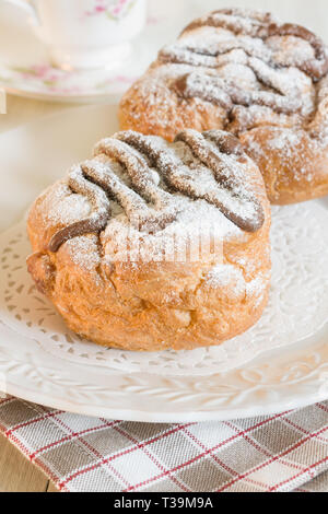 Brioches Choux rempli de crème et arrosé de sauce au chocolat et sucre glace Banque D'Images