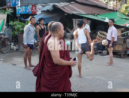 Deux moines en passant devant les hommes jouant Chinlone aussi connu comme caneball, est la traditionnelle, sport national du Myanmar (Birmanie). Il est non-compétitif, avec une Banque D'Images