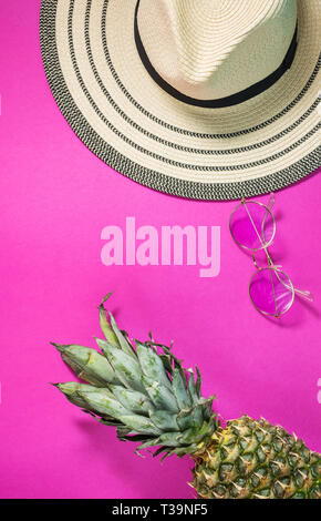 Ananas mûrs avec des lunettes de soleil et chapeau sur fond rose. Locations de concept. Vue d'en haut Banque D'Images