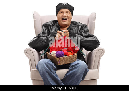 Un homme âgé dans un manteau de cuir assise sur un fauteuil et le tricotage isolé sur fond blanc Banque D'Images