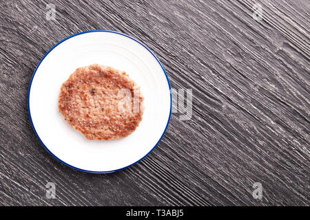 Escalope de veau sur une plaque blanche avec un anneau bleu. Sur une table en bois texturé noir. Espace libre pour la conception et le lettrage. Banque D'Images
